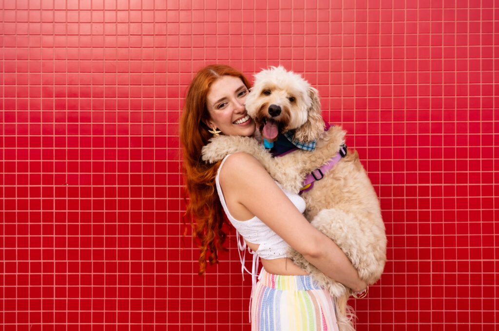 Goldendoodle Being Hugged By A Woman Against A Red Wall