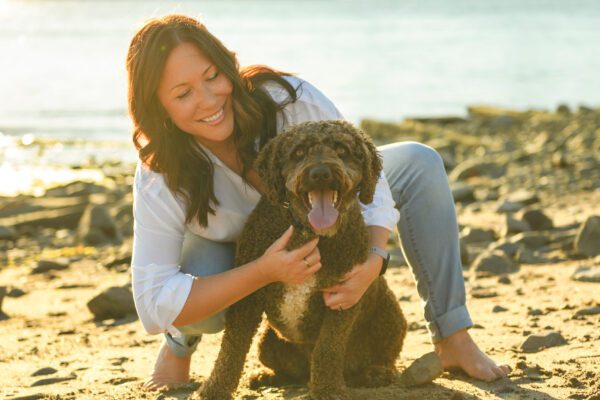 Portuguese Water Dog Sitting With Owner On Rocky Beach