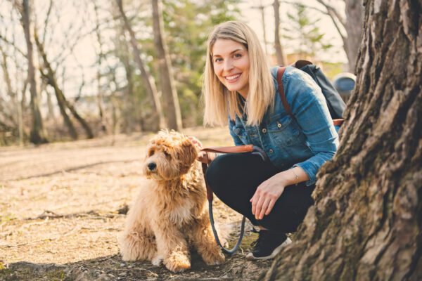 Woman Kneeling Beside A Mini Labradoodle Outdoors