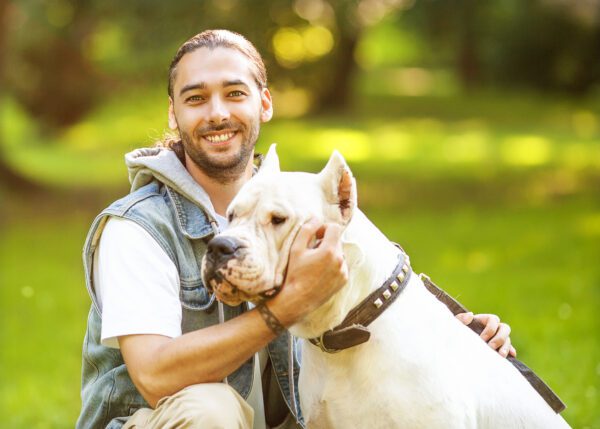 Breed Dogo Argentino Being Held By A Smiling Man In A Sunny Park