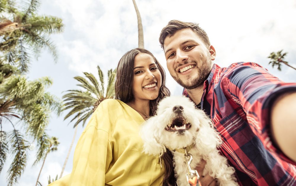 Couple holding white dog in front of palm trees