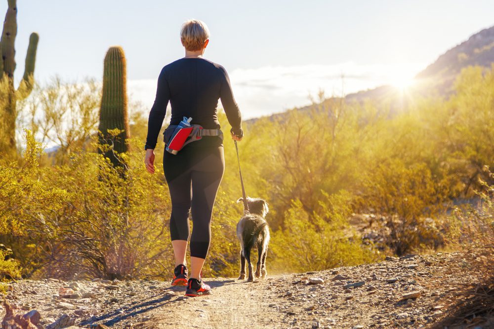 Woman walks a small dog along a desert hiking path